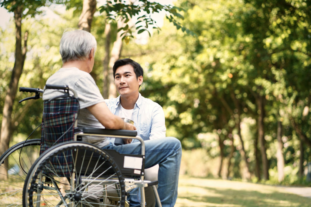 asian son talking to and comforting wheelchair bound father